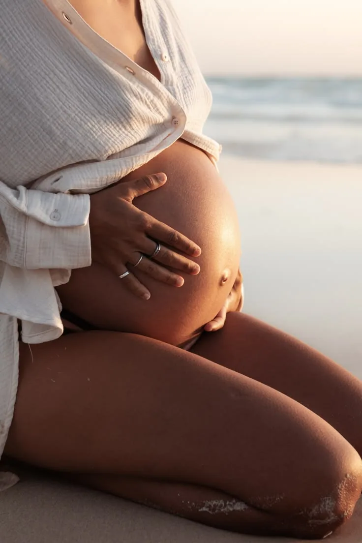 Mujer embarazada con las manos sobre el vientre junto al mar